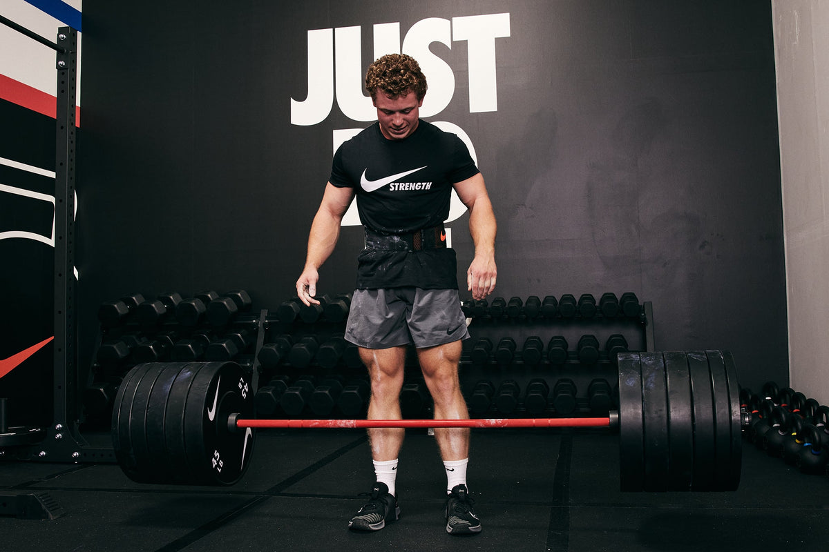 Strong male athlete dropping the Nike Coated Premium Barbell 20kg with Nike Rubber Bumper Plates